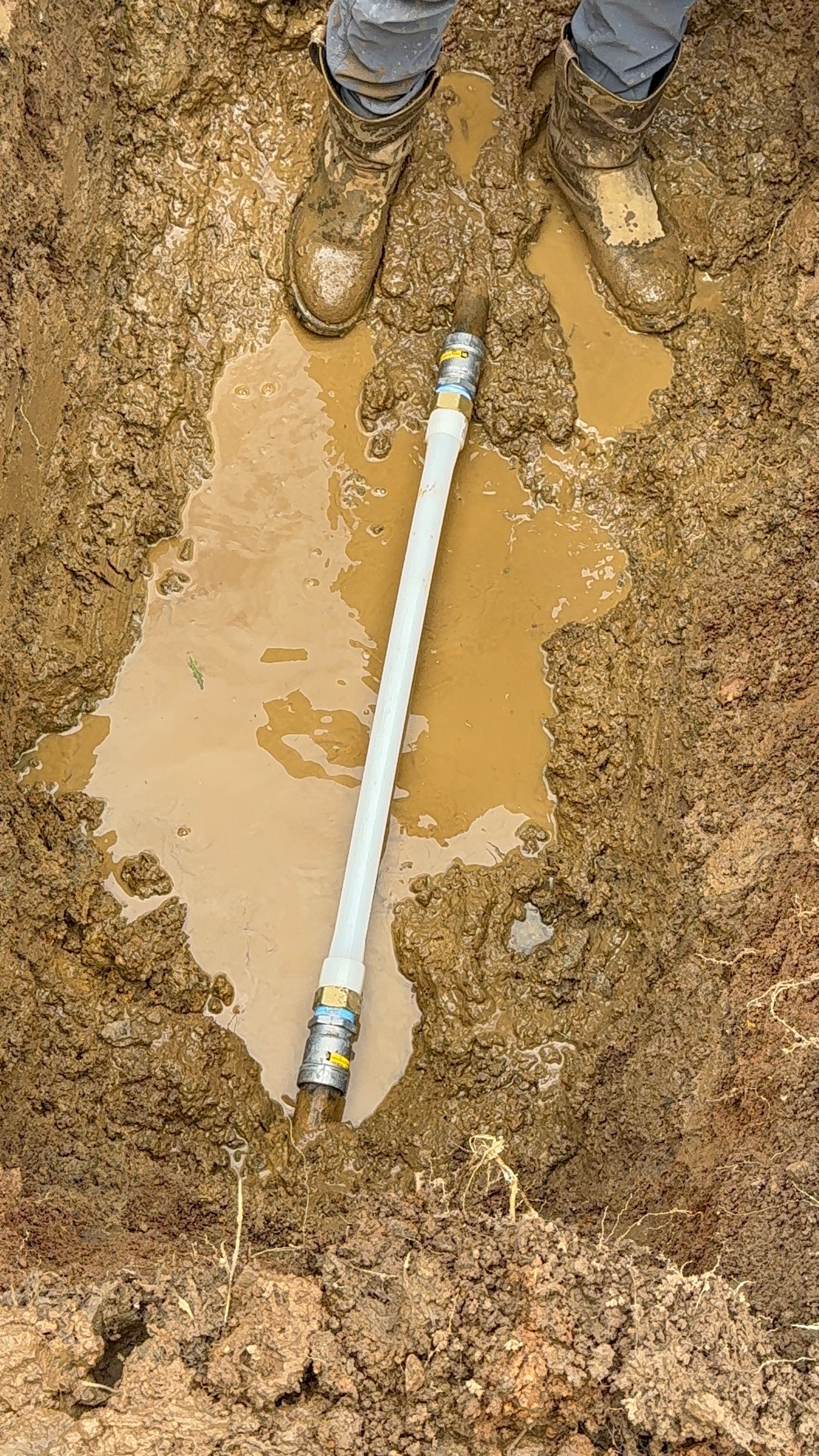Muddy utility line repair with white pipe installed in trench