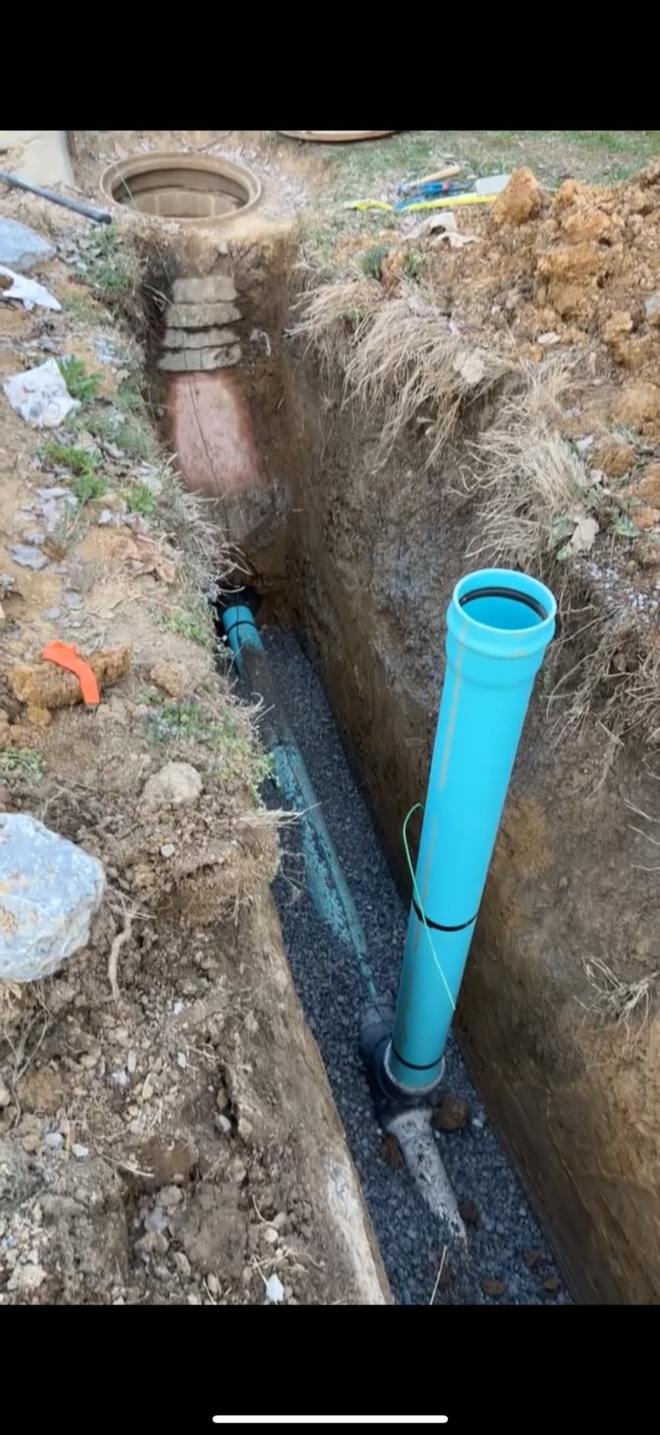 Excavated sewer line installation with blue vertical pipe